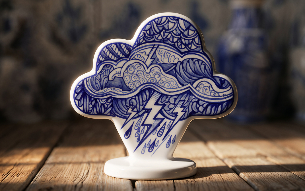 Blue and white ceramic cloud figurine decorated with storm patterns, lightning bolts, and raindrops on a wooden surface.